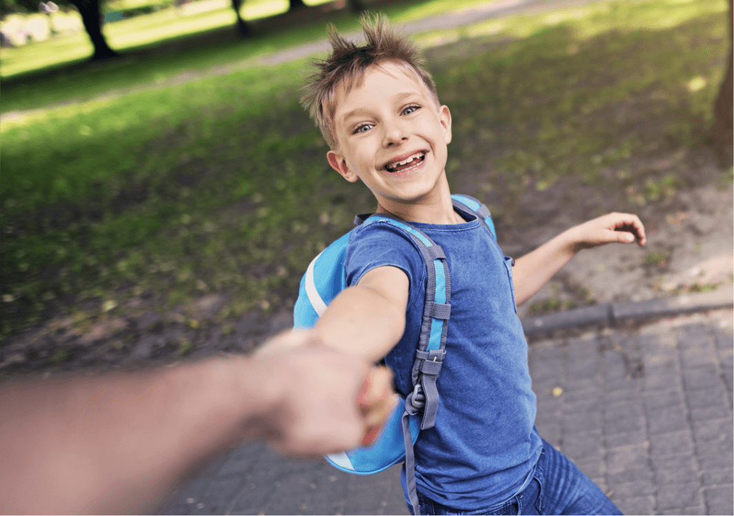 A child smiling and holding his caregiver's hand